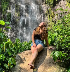 woman sitting on a rock in the jungle in front of a waterfall